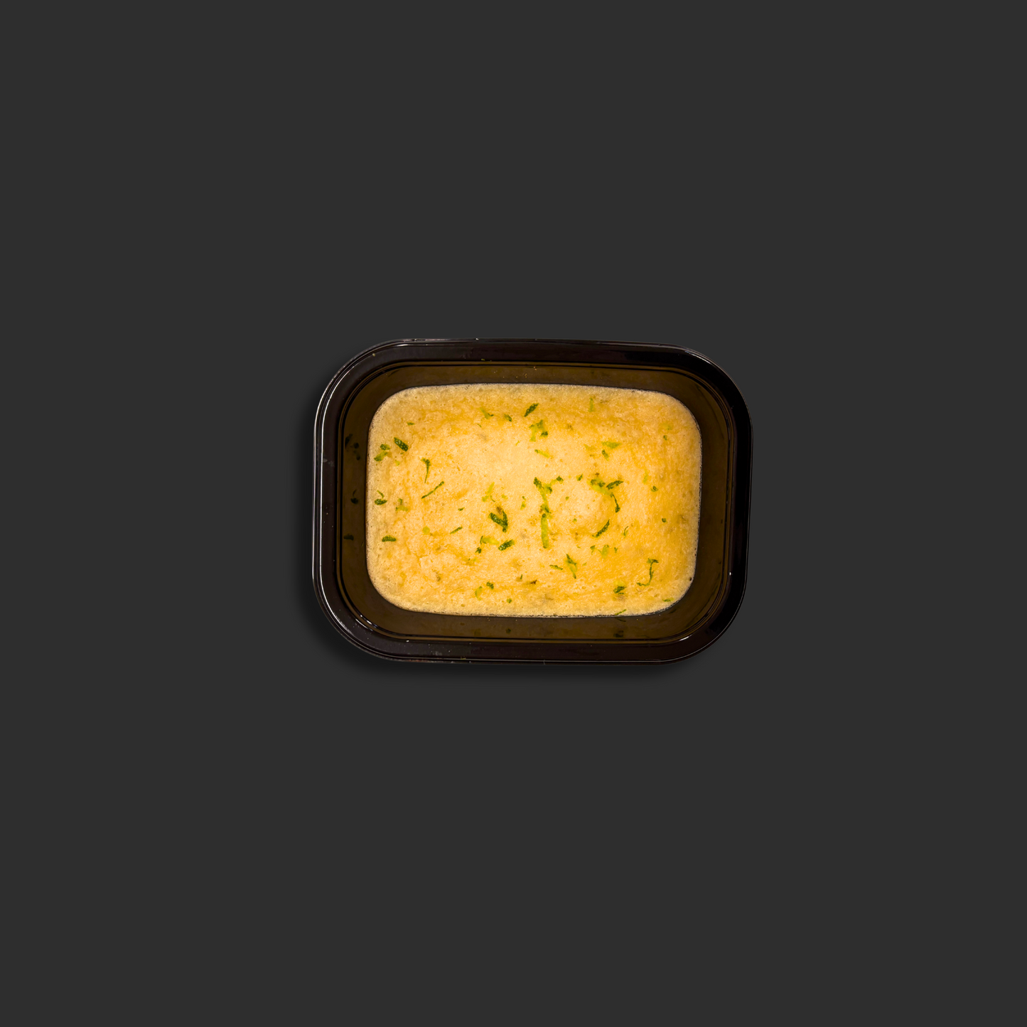 Baked lime cheesecake served in a black ready meal container with lime grated garnish and biscuit base