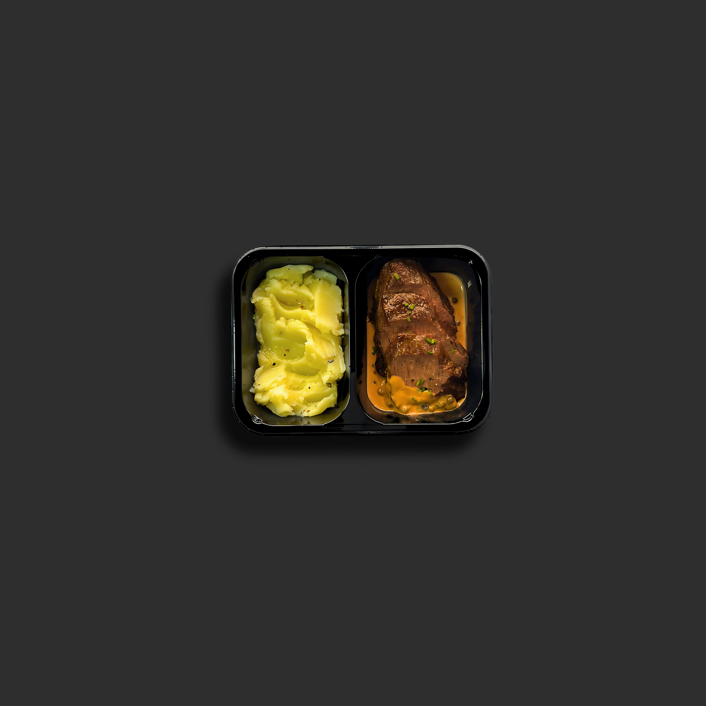 Eye fillet with creamy green peppercorn sauce in a black ready meal container with buttery mashed potato in a separate compartment, showing the premium Australian grass-fed beef meal presentation
