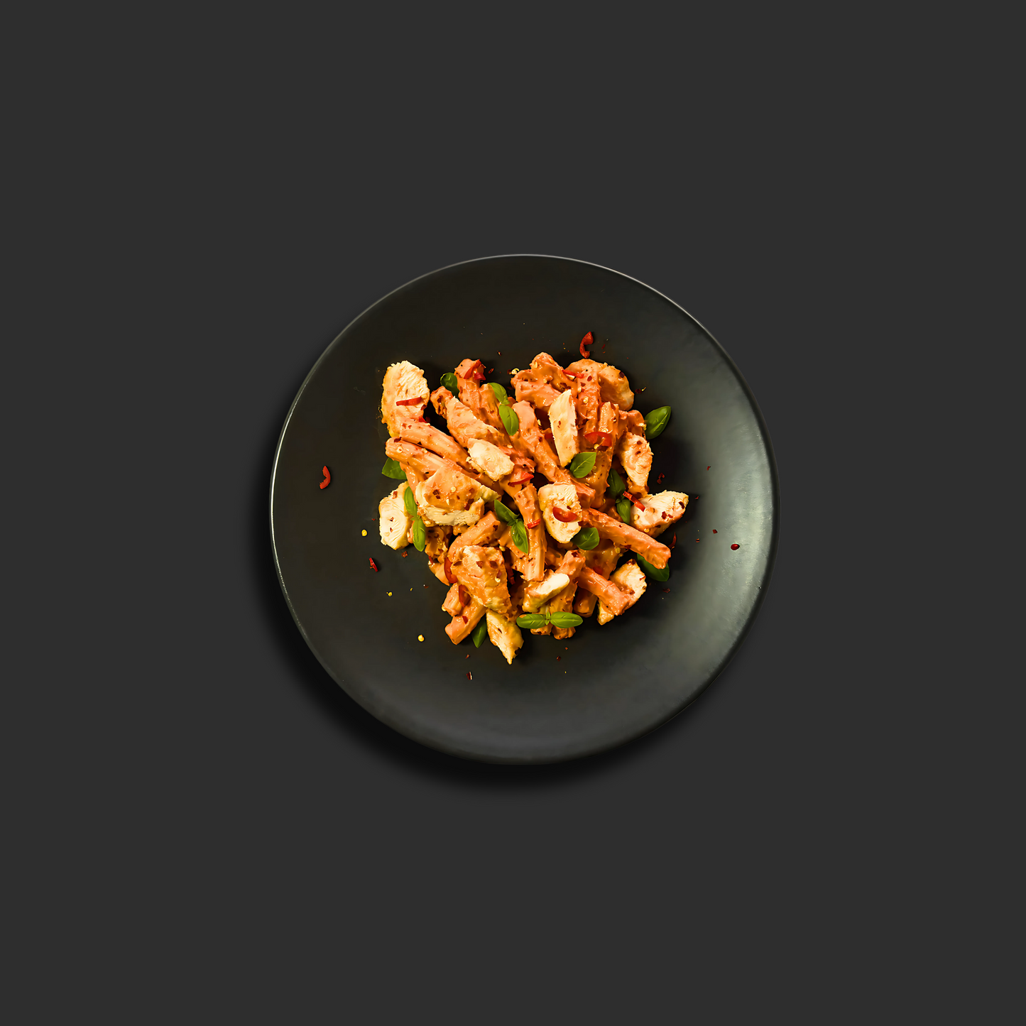 Chicken Vodka Rigatoni with tender chicken and rigatoni pasta in creamy tomato vodka sauce, garnished with fresh basil and chili flakes on a black plate.