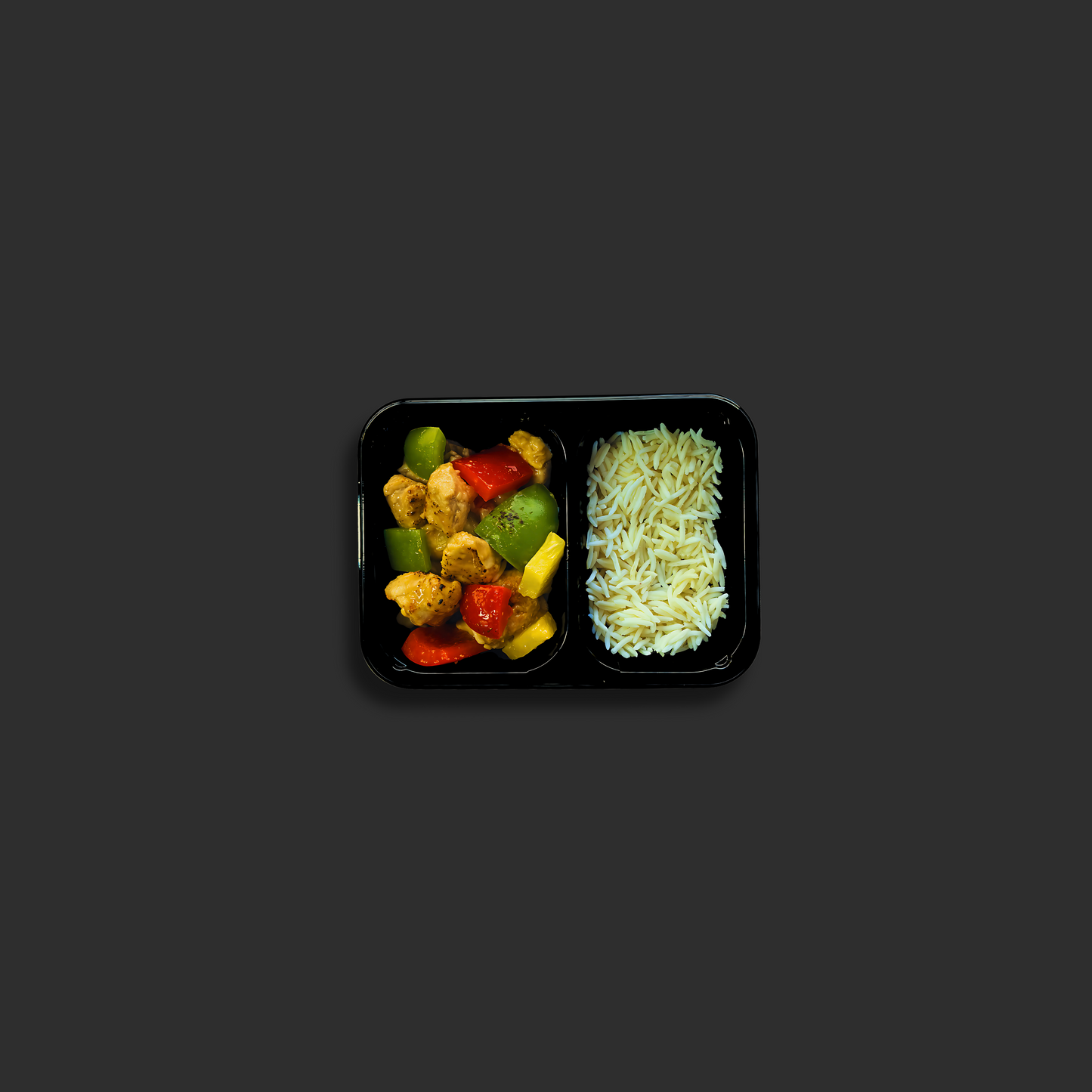 Sweet and sour pork served in a black ready meal container with compartment 1 containing pork and vegetables, and compartment 2 containing steamed white rice