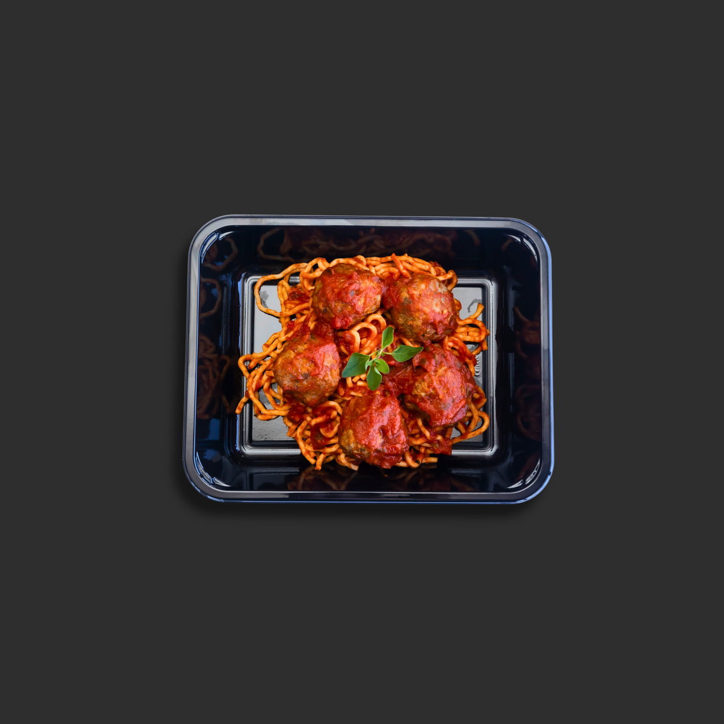 Spaghetti and meatballs Napolitana served in a black ready meal container with beef meatballs on top of pasta in Napolitana sauce and basil garnish