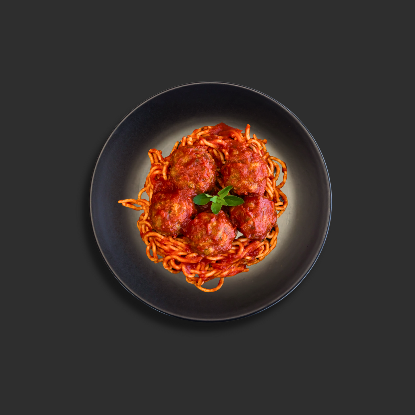 Spaghetti and meatballs Napolitana with premium beef meatballs served on top of spaghetti in Napolitana sauce, with basil garnish in the middle on a black plate