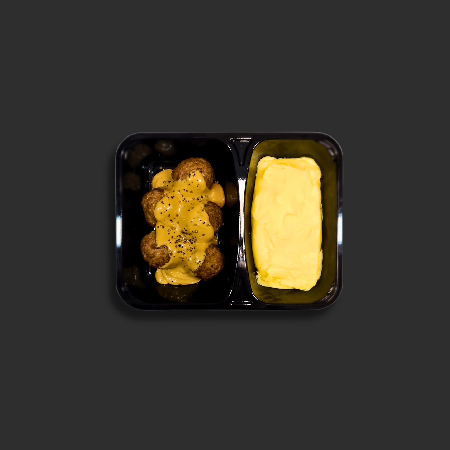 Swedish meatballs served in a black ready meal container with compartment 1 containing meatballs in gravy , cracked pepper and compartment 2 containing mash potato