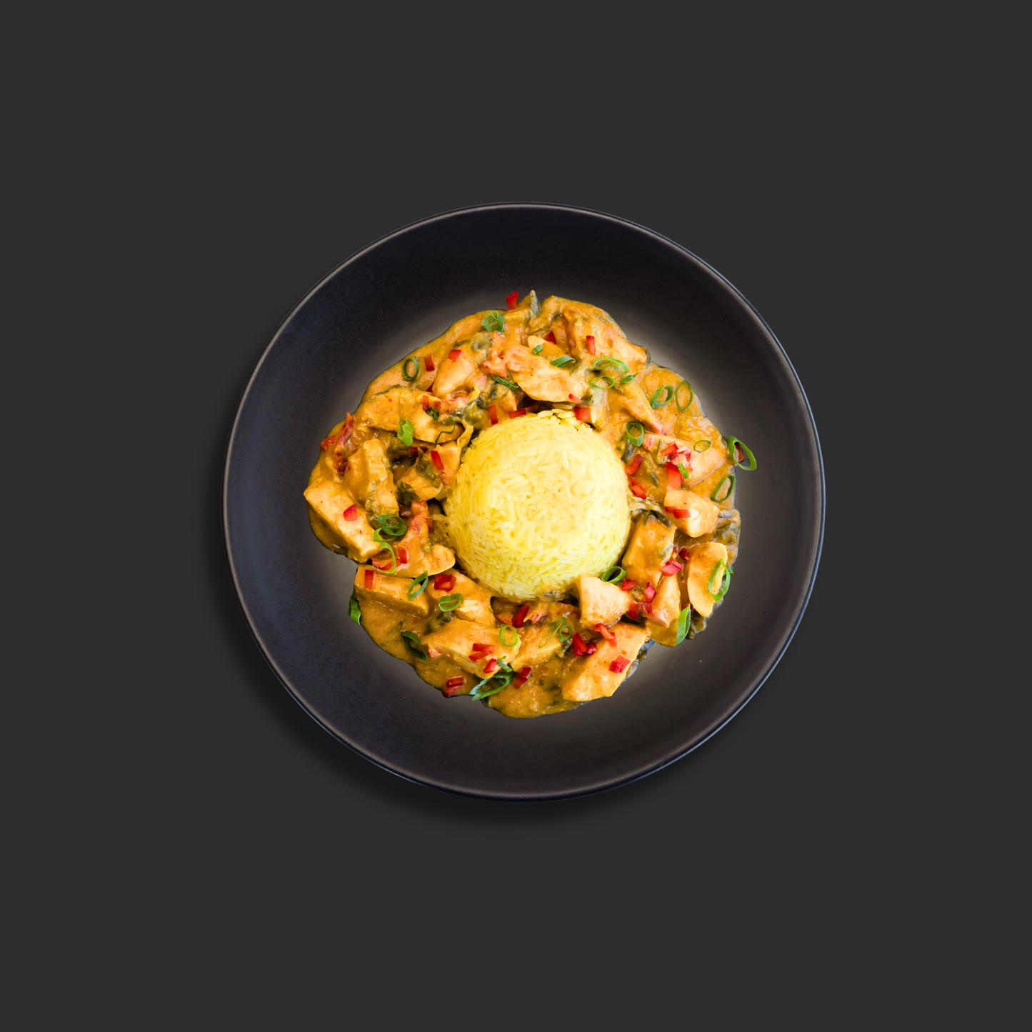 Thai yellow chicken curry with seasoned chicken tenderloin in coconut cream yellow curry sauce, served around saffron infused steamed rice on a black plate
