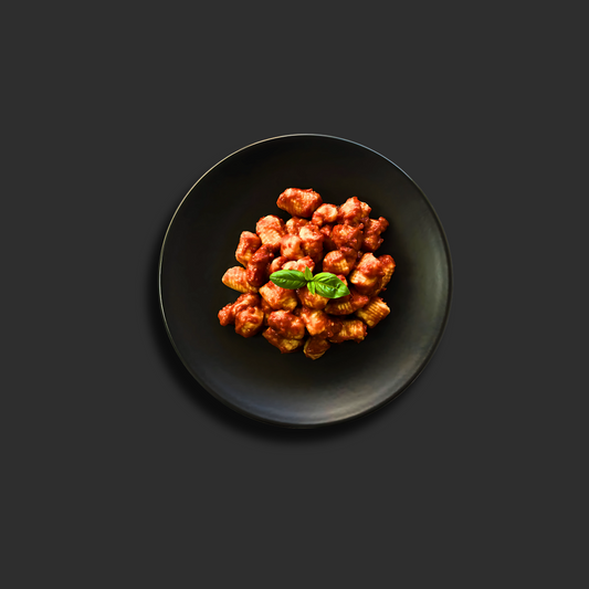 Gnocchi Napolitana with tender potato dumplings in rich tomato sauce, garnished with fresh basil and grated parmesan cheese on a black plate