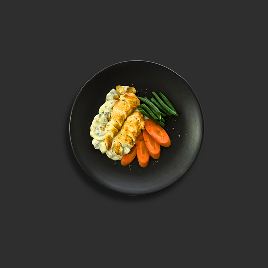 Seasoned chicken tenderloin in creamy mushroom, thyme, and white wine sauce, served with steamed carrots and beans on a black plate
