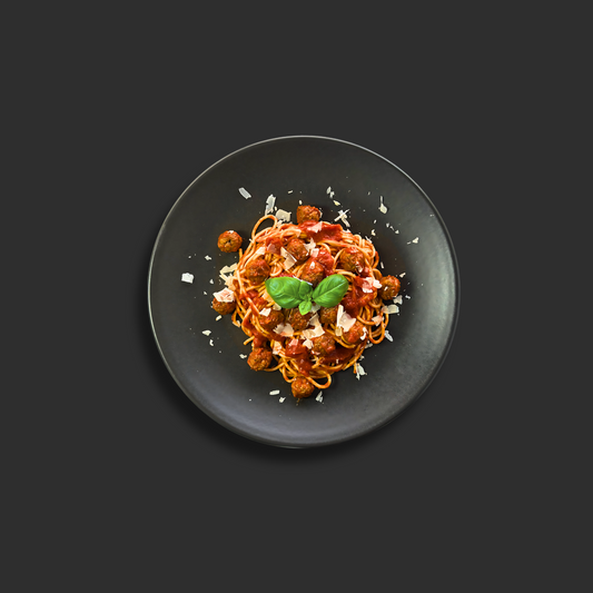 Spaghetti and meatballs with Napolitana sauce, fresh herbs and parmesan cheese on a black plate with basil garnish
