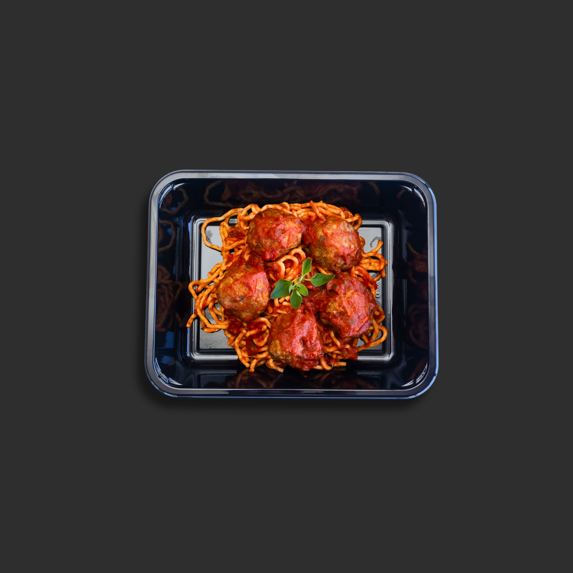 Spaghetti and meatballs Napolitana served in a black ready meal container with beef meatballs on top of pasta in Napolitana sauce and basil garnish