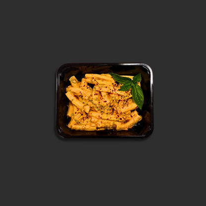 Vodka Rigatoni served in a black ready meal container with pasta in creamy tomato vodka sauce, chili flakes and basil garnish in the corner.