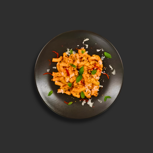 Vodka Rigatoni with rigatoni pasta in creamy tomato vodka sauce, garnished with fresh basil, chili flakes and grana Padano on a black plate.